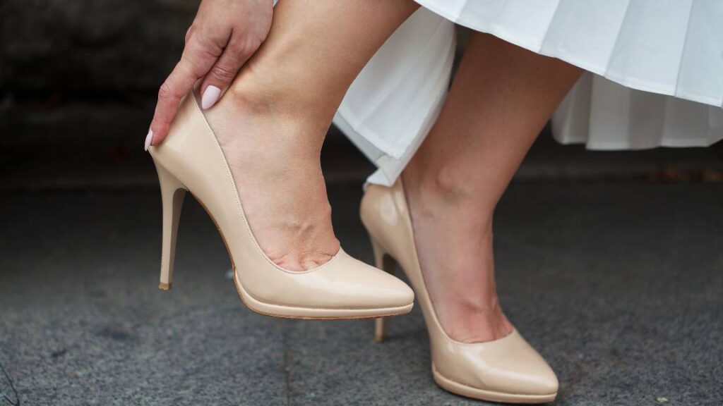Detalle de pies con calzado de tacón tipo stiletto y manos ajustando el zapato debido a presión o roce en el talón.